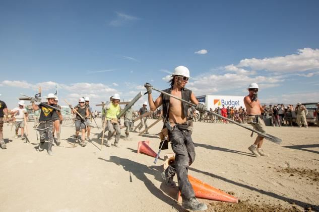 Certains membres armés d’outils, portant des casques de chantier, courent pour défoncer la voiture précipitée au sol.